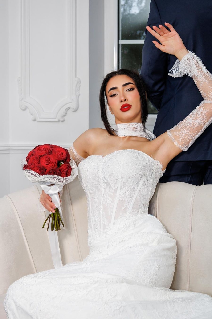 Mariée tenant un bouquet de roses rouges, manches en dentelle transparente
