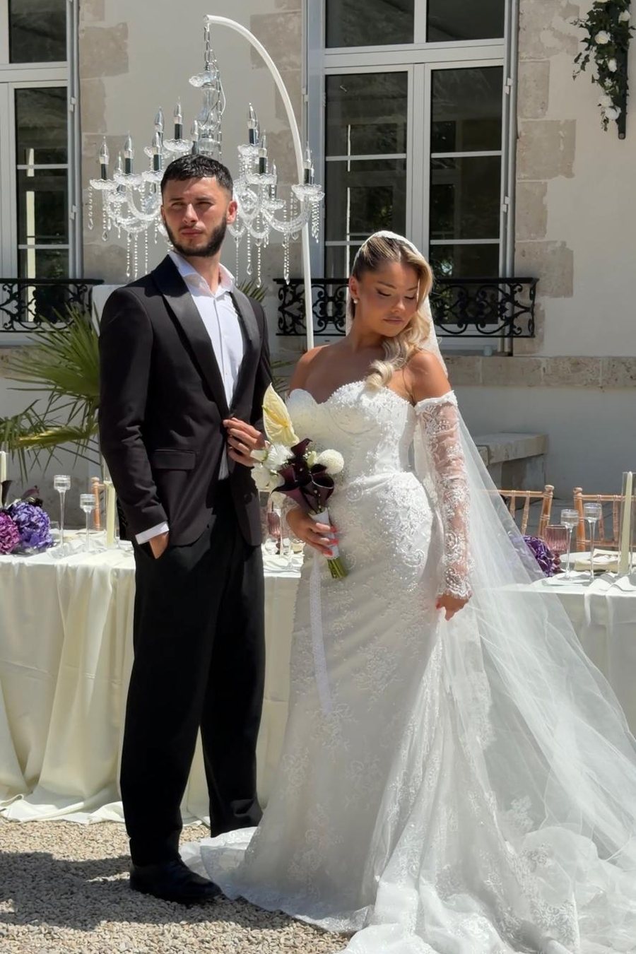 Mariés côte à côte devant la façade d'un château, table dressée en arrière-plan